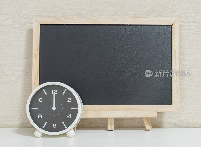 特写闹钟为装饰显示12点与木材黑色板在白色的木书桌和奶油色壁纸纹理背景，选择焦点在时钟