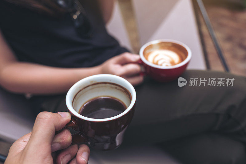 两个人坐在和拿着咖啡杯在现代咖啡馆的特写图像