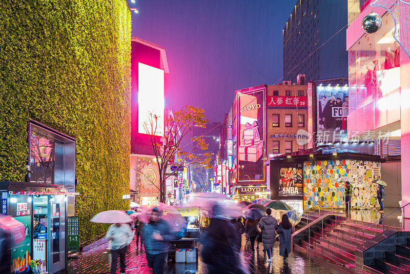 韩国首尔的明洞购物街，人们在雨天的夜晚撑着雨伞行走