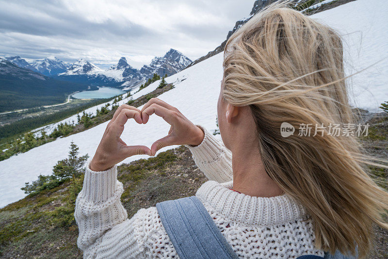 年轻女子在山湖上做心形手指架