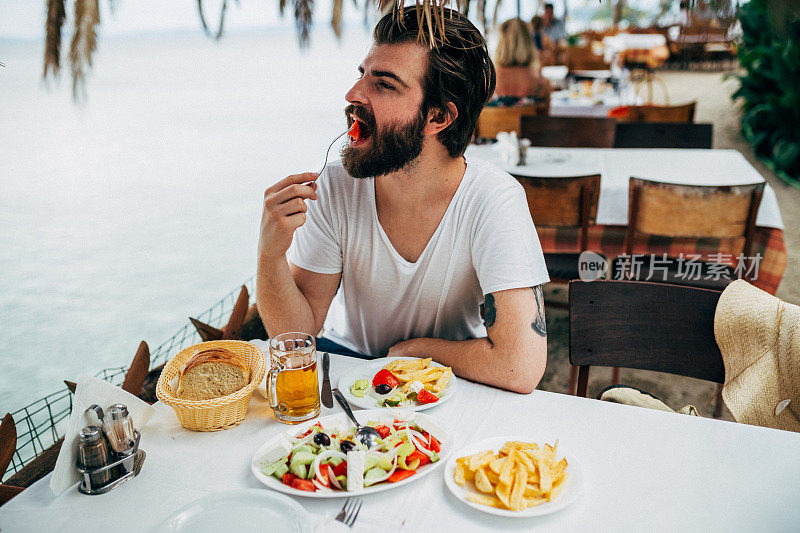 在希腊海边的一家餐馆里，一位英俊的大胡子正在用餐