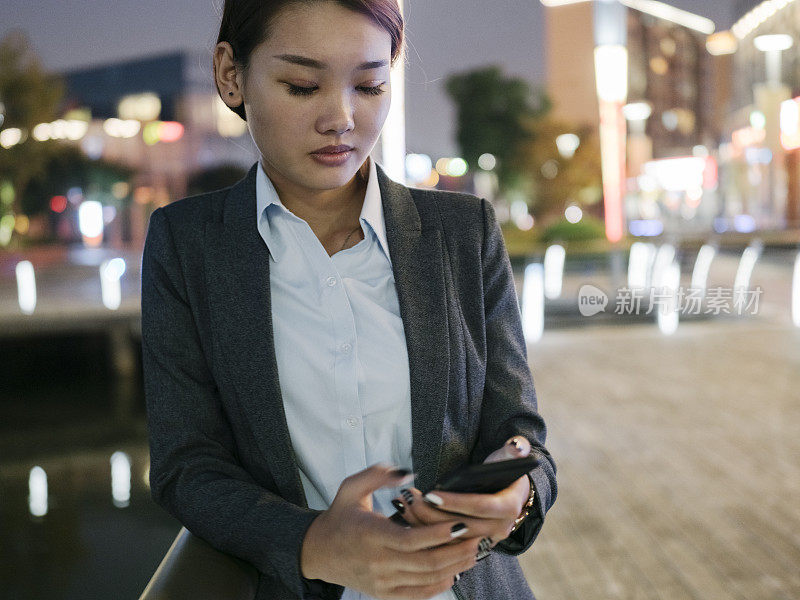 商业女性拿着智能手机和手提包站在城市里的肖像
