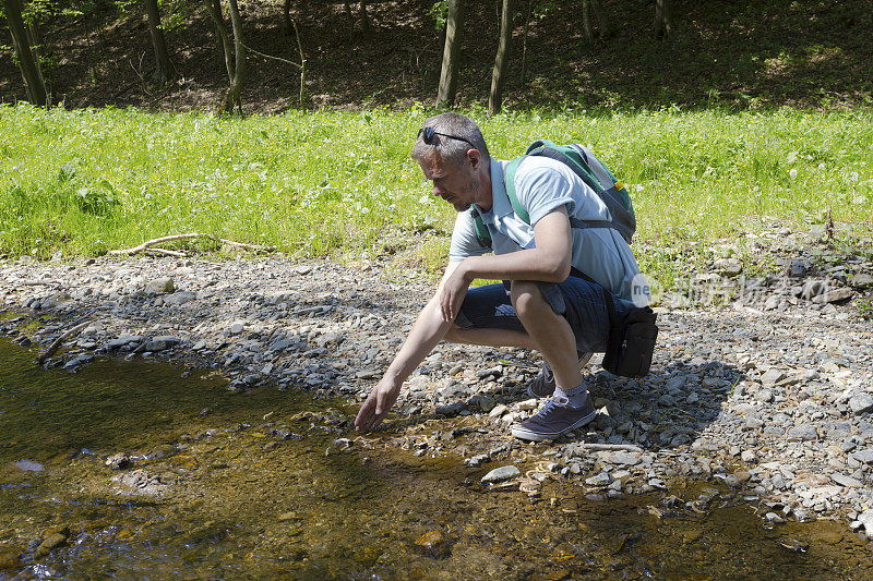成年徒步旅行者用小溪的水提神