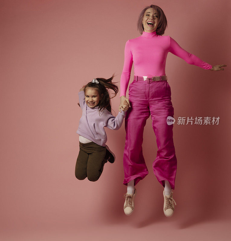 母女二人最好的友谊跳跃在空中演播室前拍摄粉红色的背景