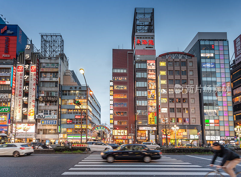 新宿镇晚上的街道上挤满了等待人行横道的人。新宿是位于东京的一个夜间购物区。