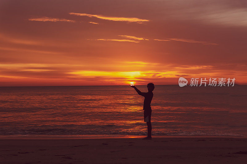 在海滩上抱着日出的少年剪影