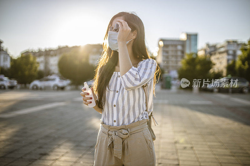 一名年轻女子戴着外科口罩，手上涂着洗手液，在封锁期间站在空荡荡的城镇广场上