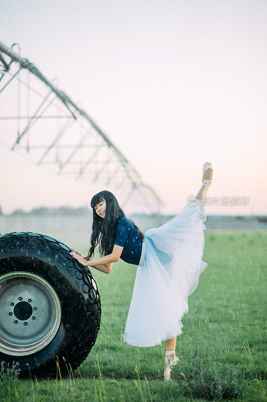 一名芭蕾舞演员在农用喷雾器的轮子旁边表演燕子姿势。