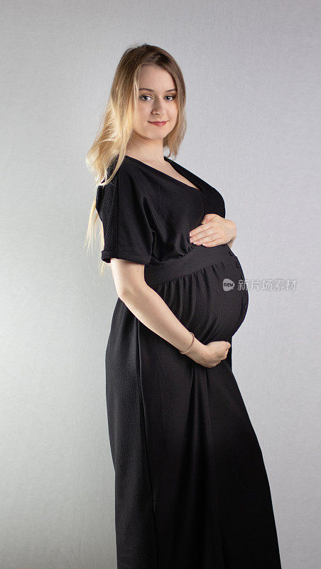 这是一幅漂亮的年轻孕妇肖像，她有着金色的长发，背景是普通的中灰色。
