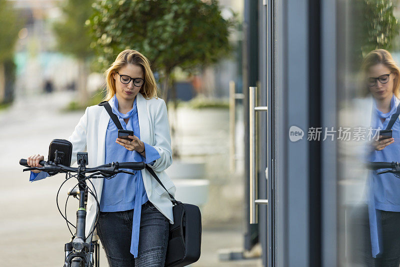 一个女商人正在上班，推着她的自行车，在电话上输入信息。