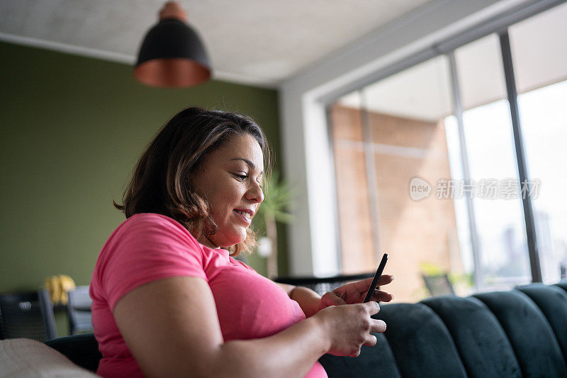 成熟女人坐在家里的沙发上玩智能手机