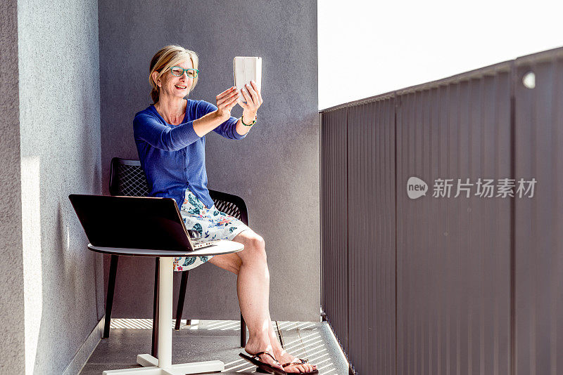 自由女性在酒店阳台上使用笔记本电脑在户外工作，并用手机进行视频通话