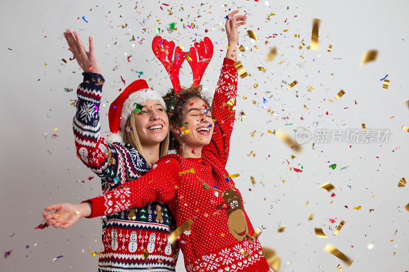 圣诞节到了!两个美丽的女人穿着圣诞毛衣，周围撒着五彩纸屑