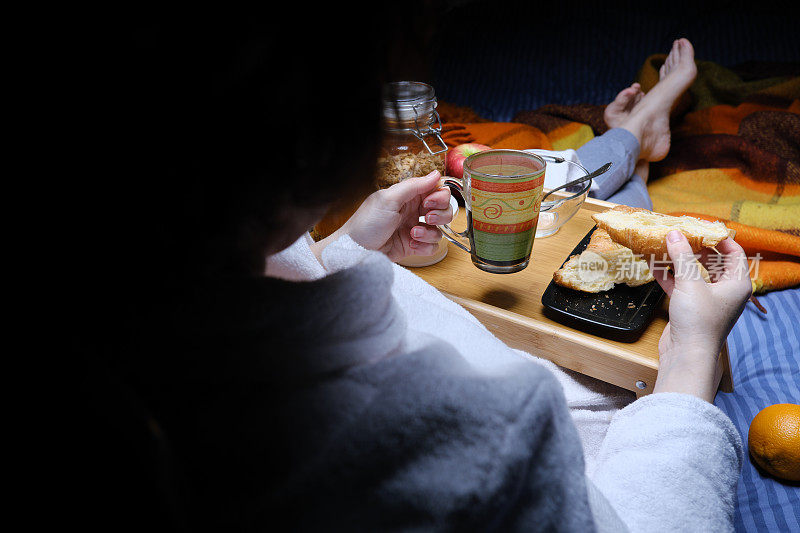 成熟的女人穿着浴衣和睡衣坐在床前吃早餐