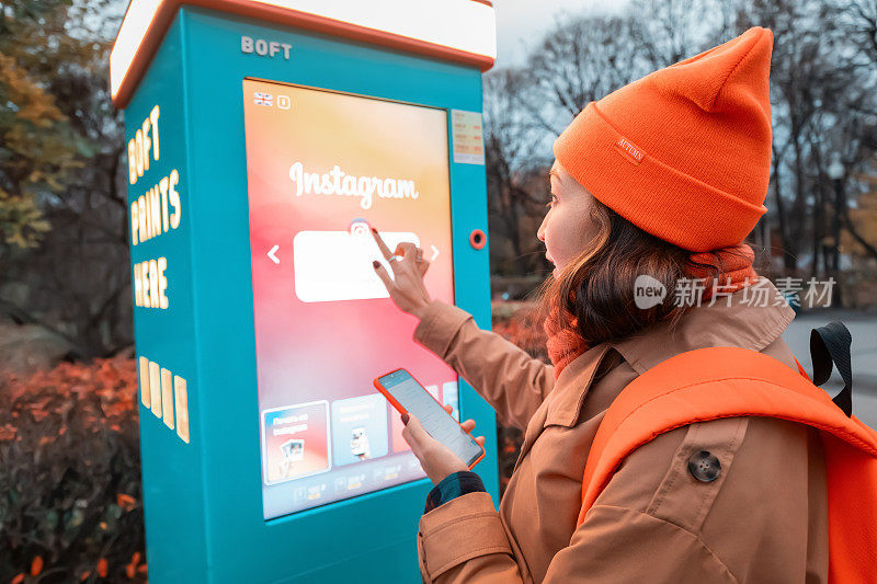 一名女子在城市街道上使用自助服务亭打印智能手机上的照片