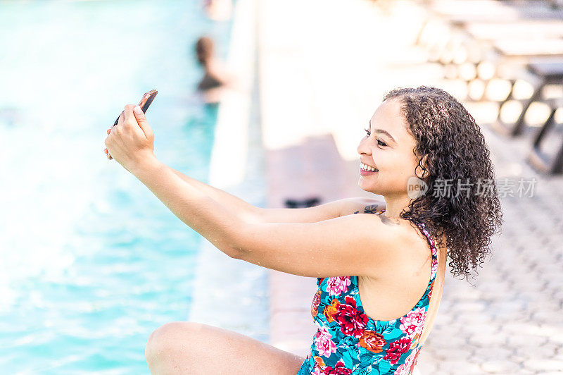 美丽的非洲裔加勒比妇女在一个户外度假游泳池放松和自拍