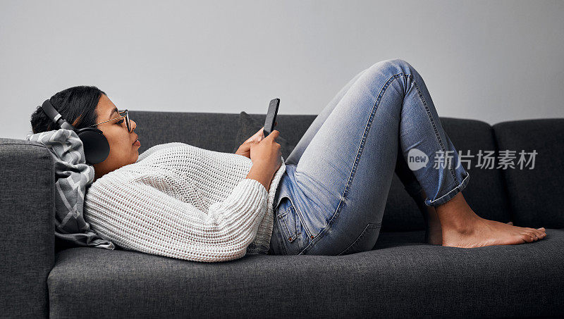 一名年轻女子在家里的沙发上使用智能手机和耳机