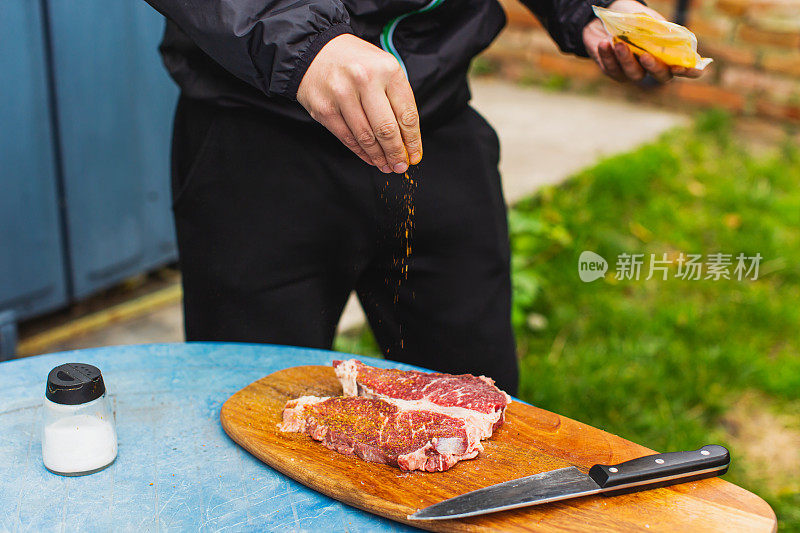 新鲜牛排。满足户外经验。晚餐在后院。木板上红肉。准备食物的过程。小牛肉。美味的小吃。户外用餐。盐和调味食品