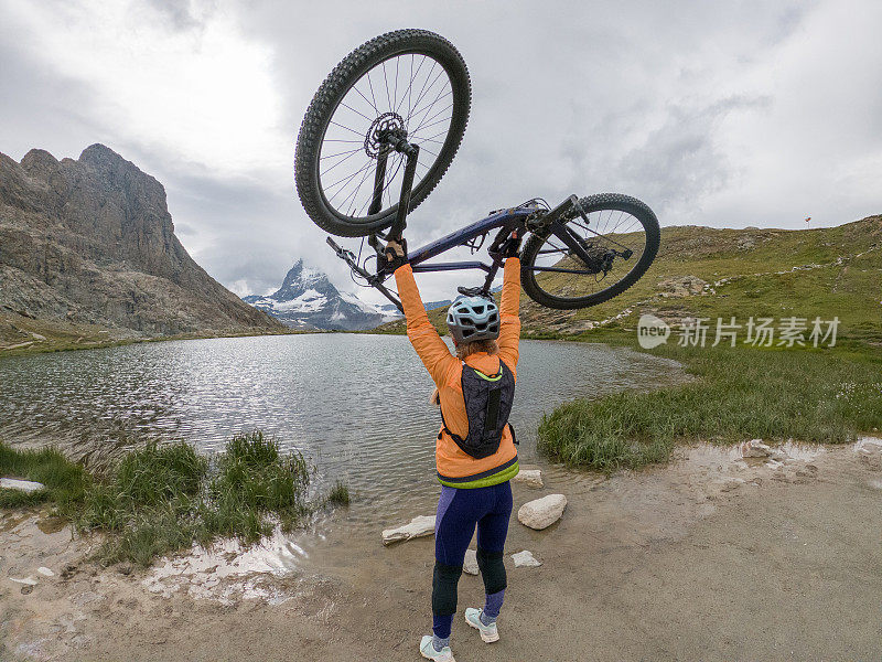 在马特洪峰下的Riffelsee湖上，一名女山地自行车手举着头顶的自行车