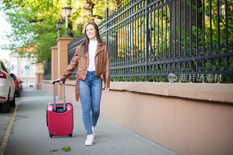 年轻的女人走着，拉着一个小的轮式行李