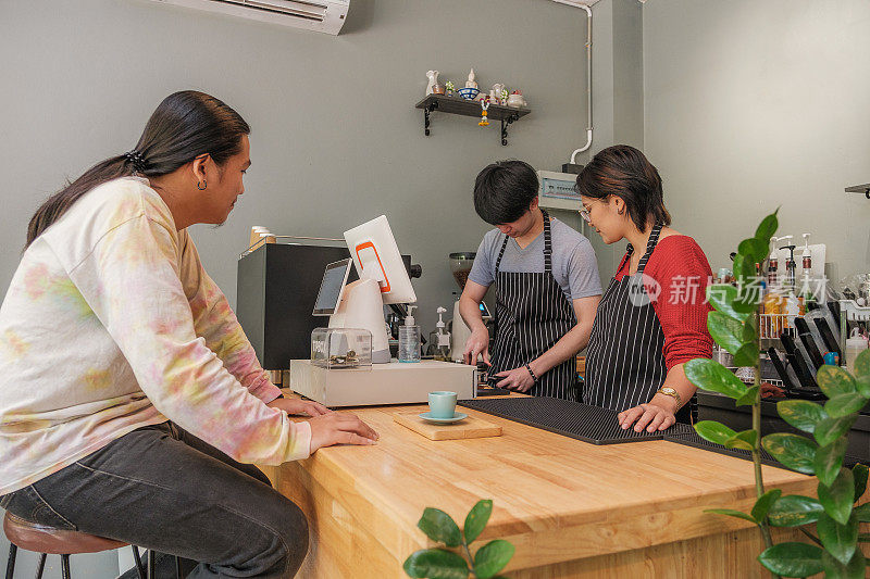 年轻的亚洲咖啡师或咖啡店老板在咖啡馆的吧台为顾客煮咖啡