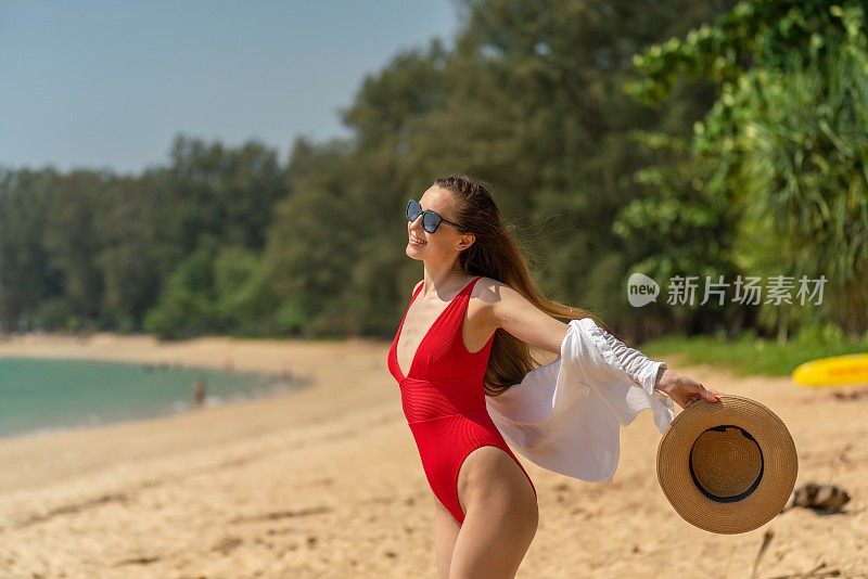 美丽的白人女性性感的女人在红色泳装比基尼海滩拿着沙滩帽戴着太阳镜笑着开心地看着大海享受海风