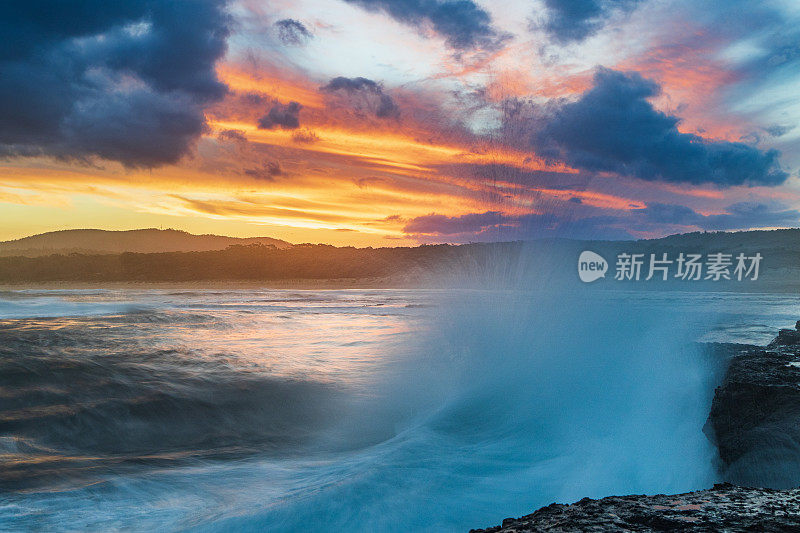 海浪拍打着岩石，海洋上的金色日落引人注目