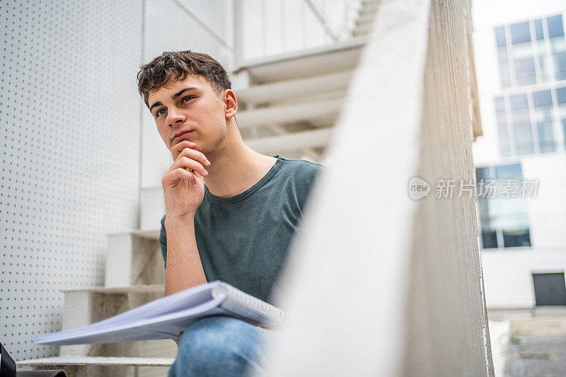 一个高中生坐在学校大楼的台阶上学习