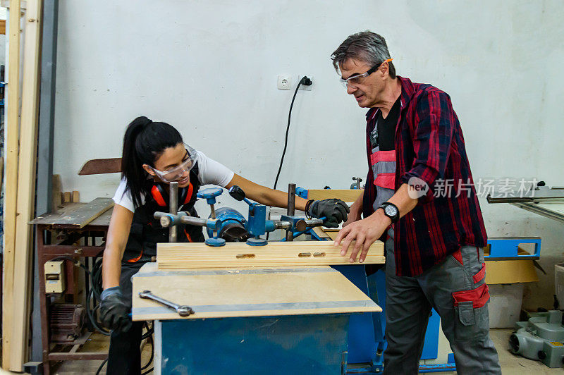 木工车间里，女木匠和她的老男同事正在使用分切机。