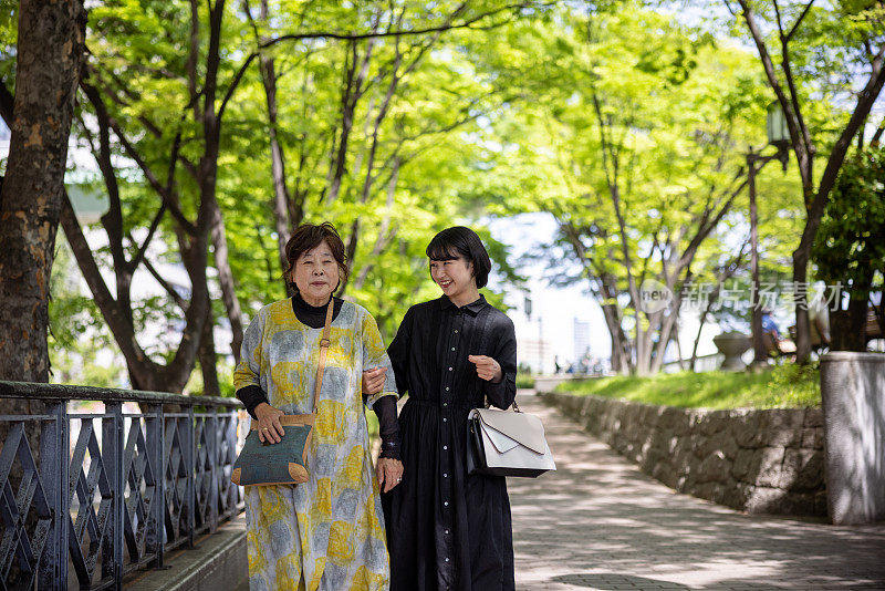 一位年轻女子和她的祖母走在绿树成荫的街道上