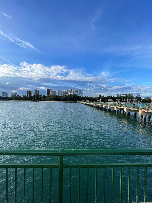 新加坡东海岸公园，多云晴朗的蓝天，碧德码头的绿色栏杆和城市景观天际线的特写照片