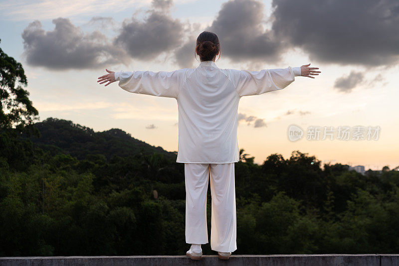 一位亚洲妇女正在公园里练习健身运动太极拳。