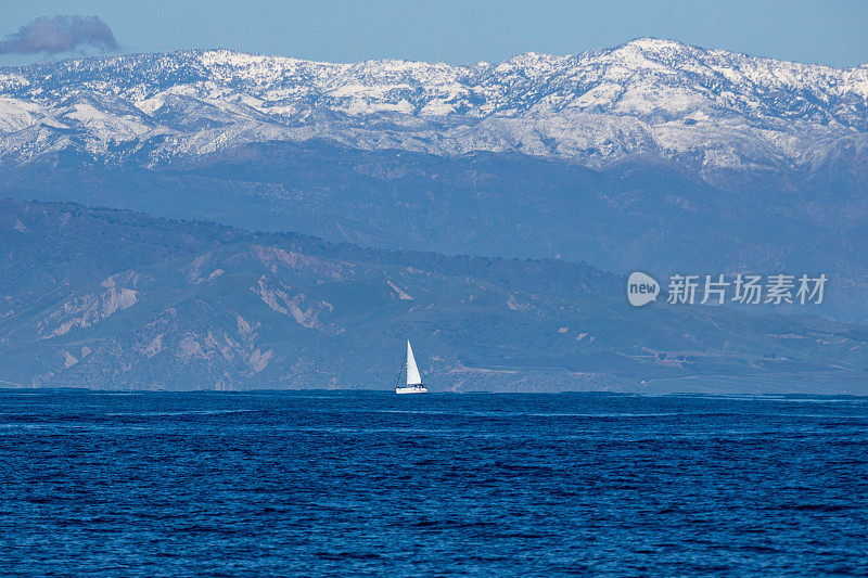 冬天，一艘小帆船驶离加州文图拉海岸，背景是托帕托帕山脉上的雪