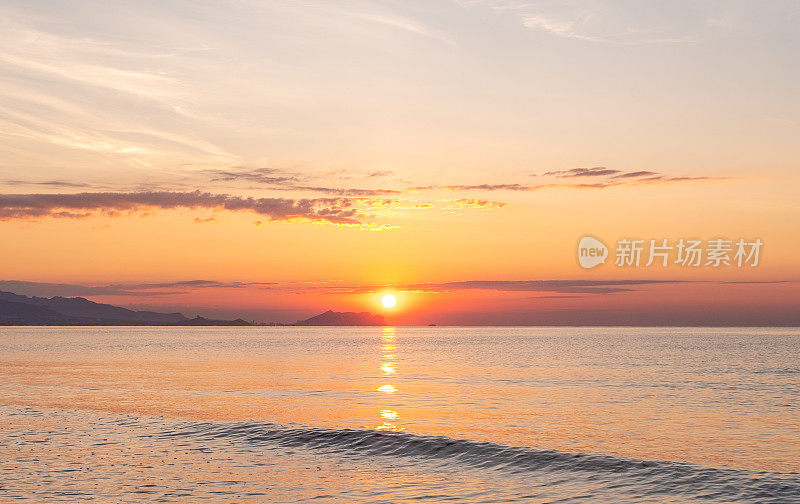 明亮的日出掠过海面，一座山在朦胧的背景中。圣胡安海滩阿利坎特