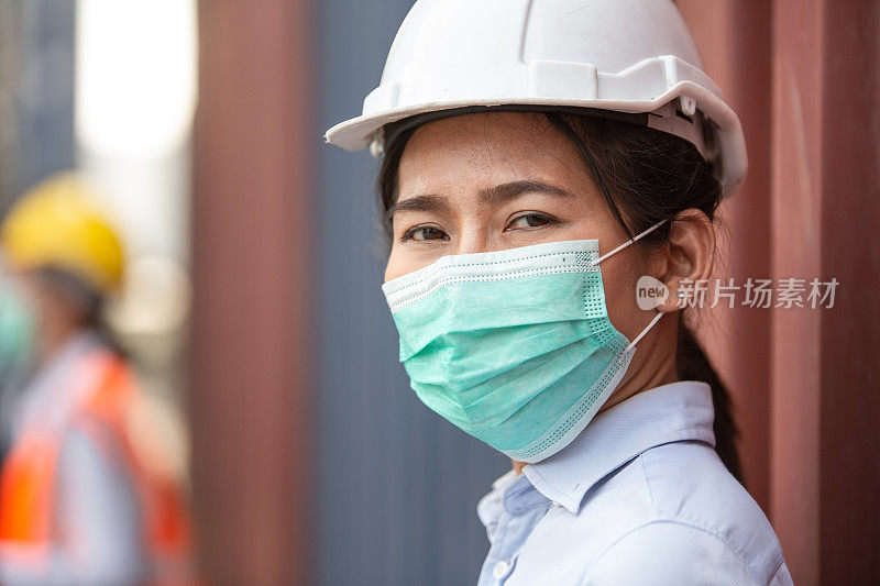 在物流货仓工作的亚洲女工戴着防护口罩看着摄像机。进出口经营理念