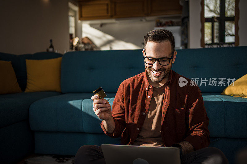 一名白人男子正在网上购物，脸上带着快乐的表情，正在使用笔记本电脑，手里拿着信用卡