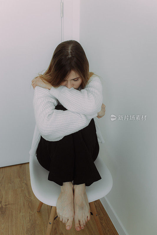 一个年轻的女孩坐在白色背景的椅子上，沉浸在她的思想中，为文字留出空间。自我认识的概念。心理治疗师和教练的视觉效果