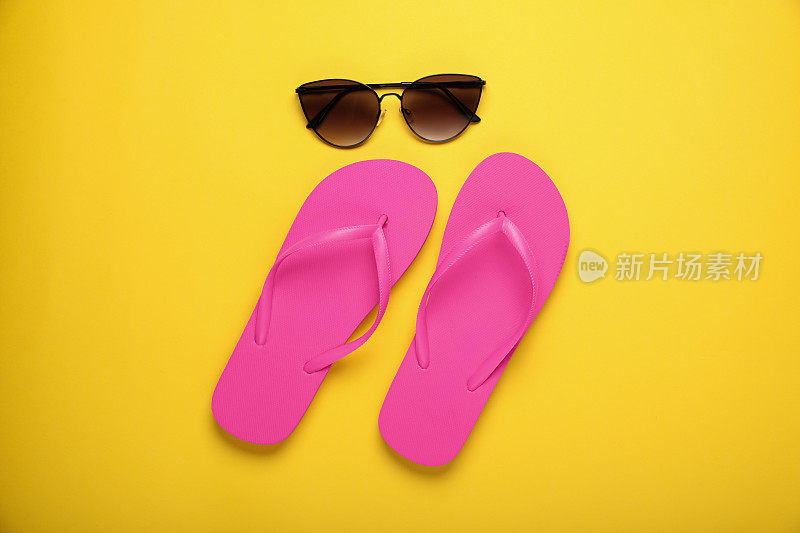 时尚的粉色人字拖和太阳镜，黄色背景，平躺