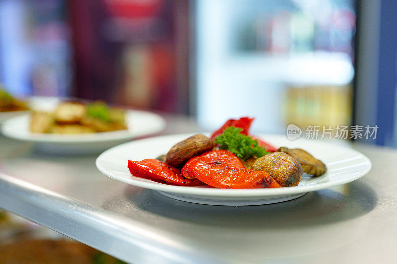 在繁忙的餐厅厨房里，白色盘子里充满活力的烤蔬菜