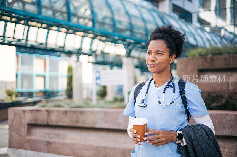 女医生站在外面，拿着咖啡杯。她微笑着享受着她的咖啡休息时间