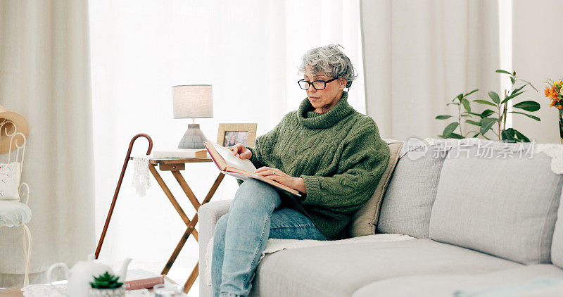 退休后的女人在客厅里读有趣的书，寻找故事、小说和知识。快乐的老年女性在休息室里看书休息，在家沙发上欣赏文学和爱好