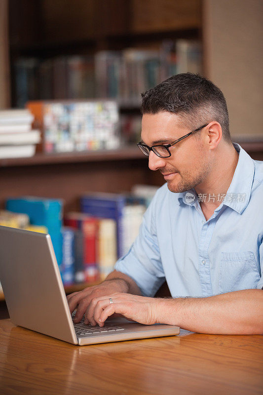 微笑的男学生在大学图书馆使用笔记本电脑