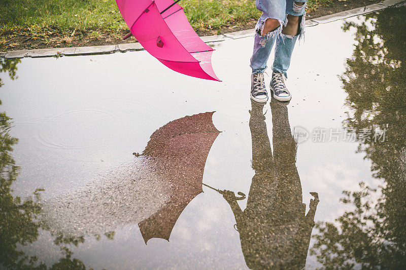 一个漂亮的女孩跳在路上的水坑里