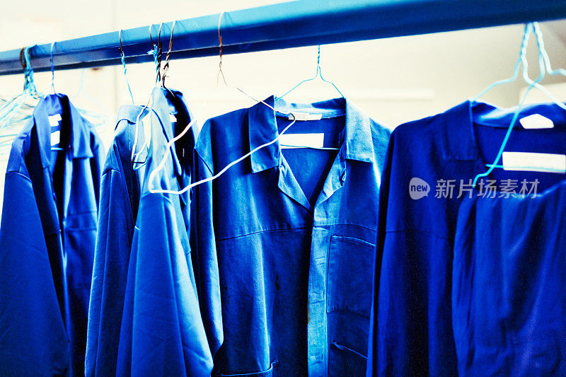 工人的蓝色工作服挂在工厂更衣室的栏杆上