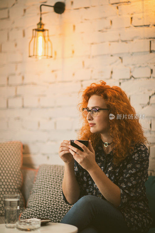 年轻的红发女人享受着一杯咖啡和思考。