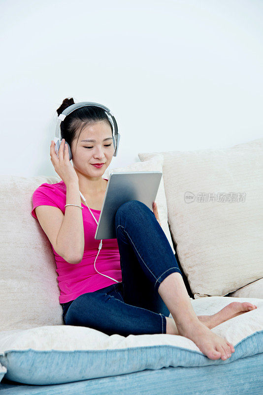 年轻女子坐在沙发上，戴着耳机和平板电脑