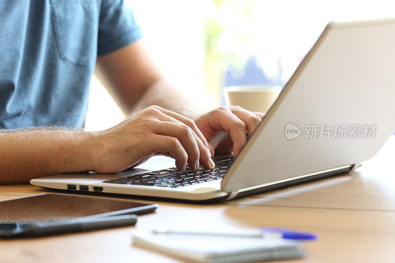 一名男子在桌上的笔记本电脑键盘上打字