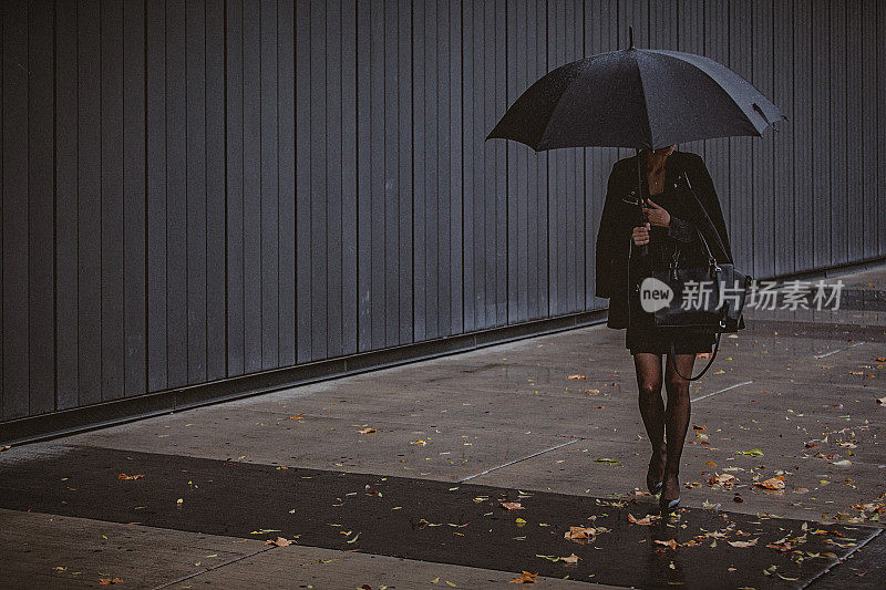 一名年轻女子撑着伞，在寒冷的秋日里在风雨中行走。