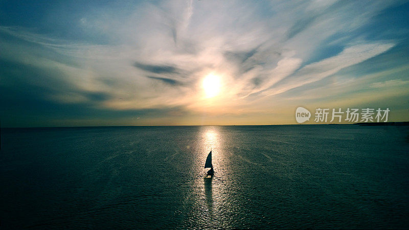 一艘白色的小船在夕阳的余晖中漂向地平线。美丽的云彩与黄色的亮点。鸟瞰图