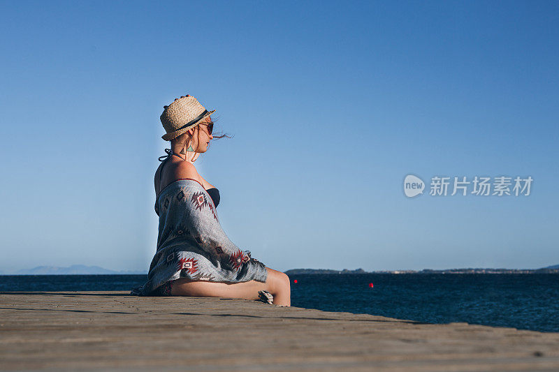 侧面的年轻女子戴着帽子坐在码头上的海滩